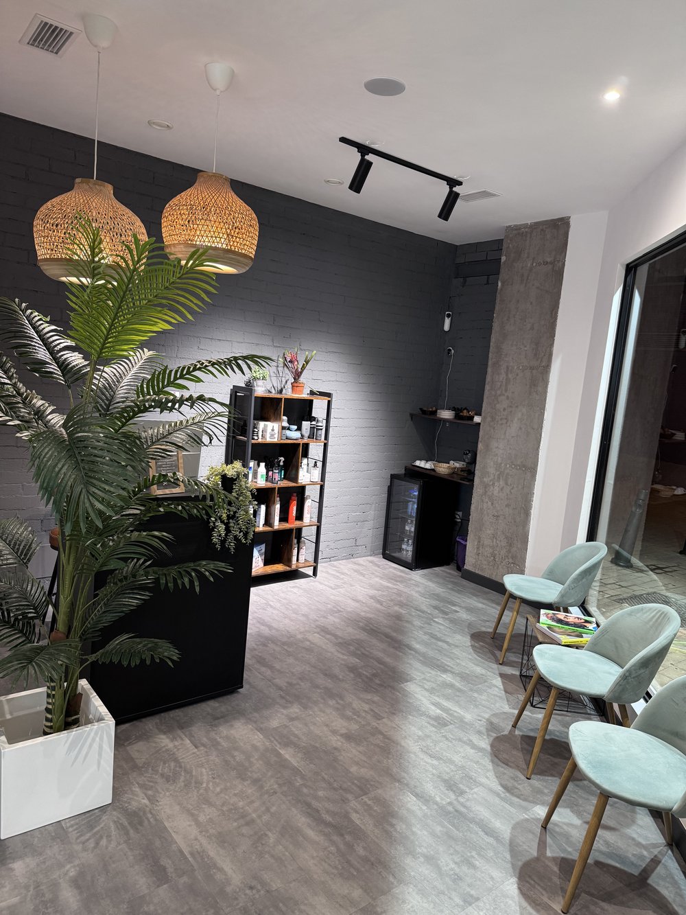 Recepción de ORIGEN Hair Studio: pared de ladrillo negro, lámparas de fibra natural y estantería con producto profesional