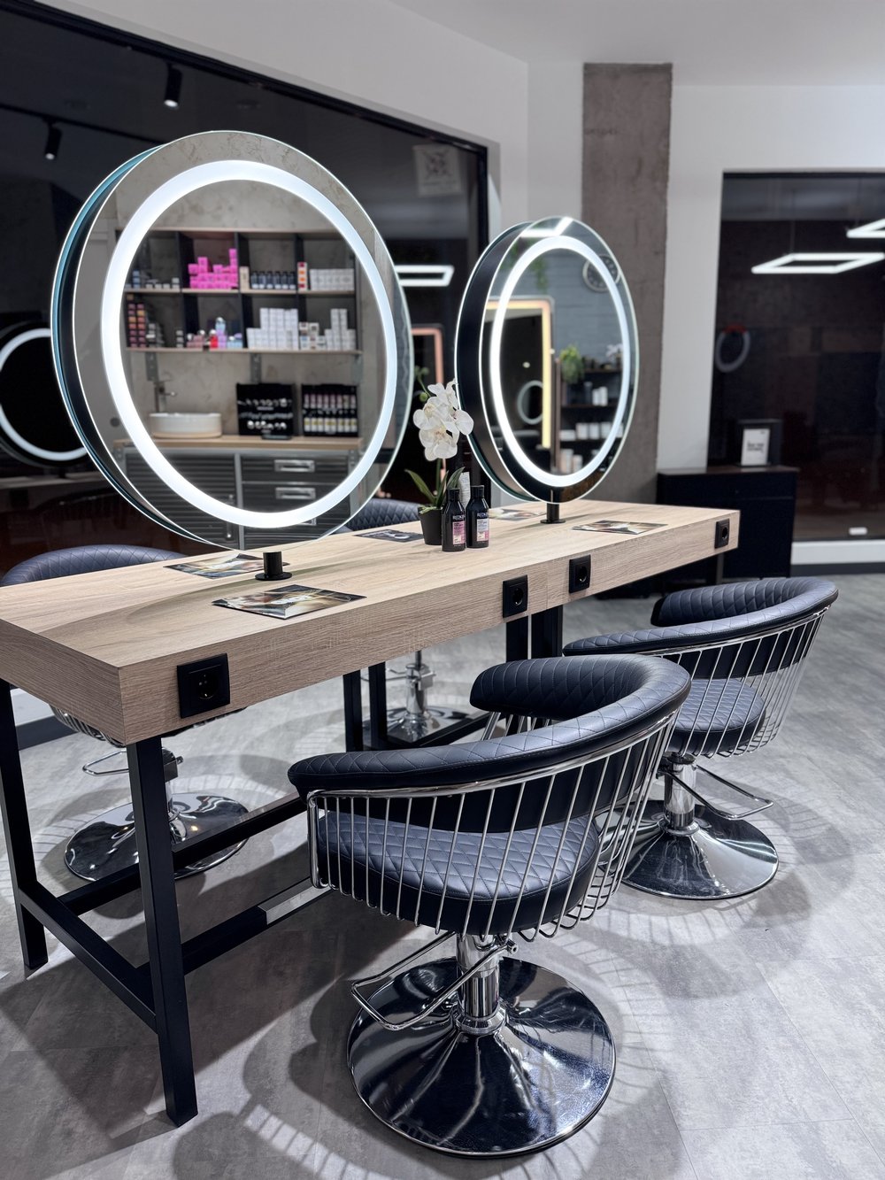 Tocadores de ORIGEN Hair Studio con espejos circulares retroiluminados y sillones negros capitoné